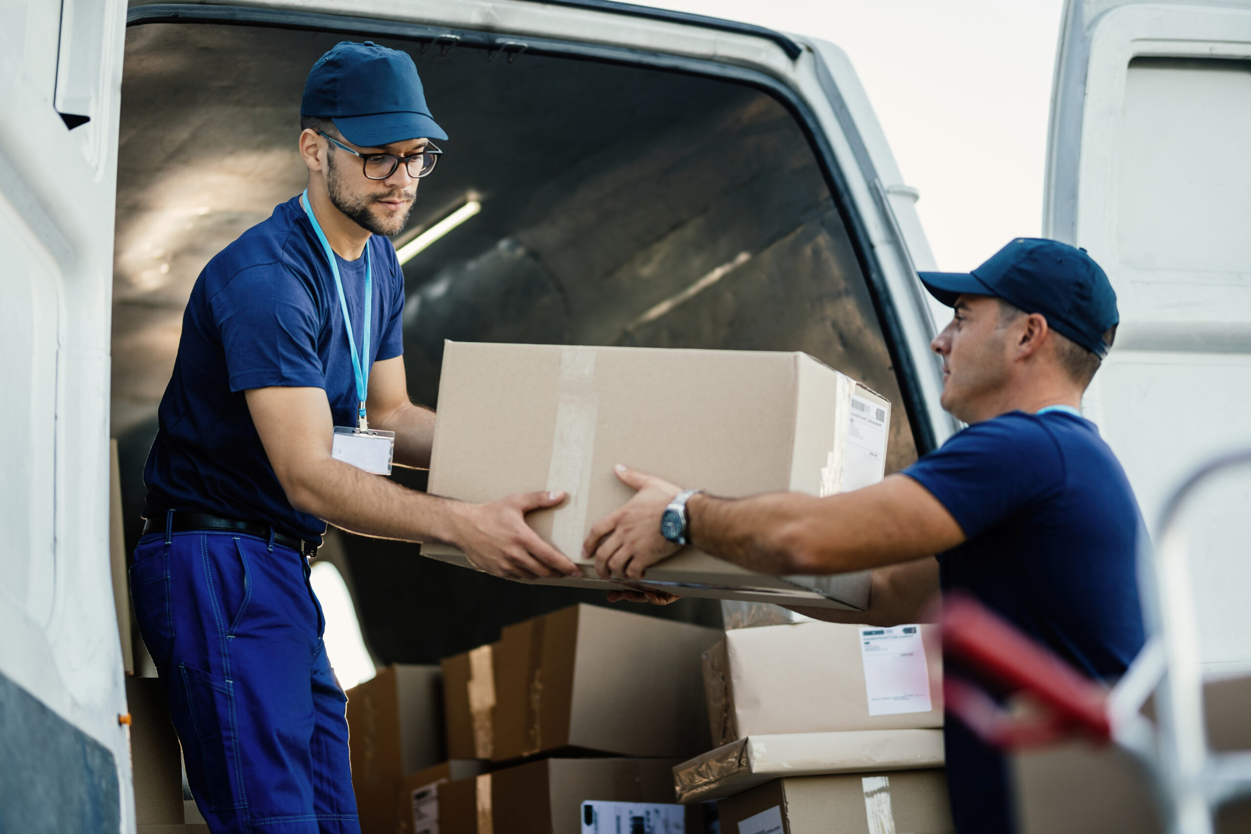 Young couriers cooperating while unloading packages from deliver